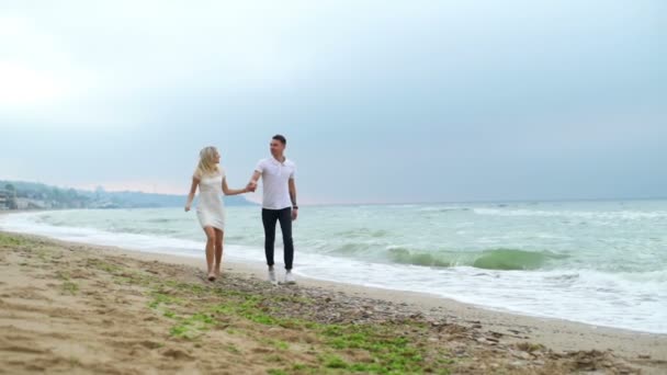 Jovem casal corre ao longo do mar, em seguida, o homem gira e beija mulher câmera lenta — Vídeo de Stock