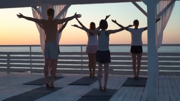 Grupo de pessoas praticar ioga no terraço perto do mar ao amanhecer câmera lenta — Vídeo de Stock