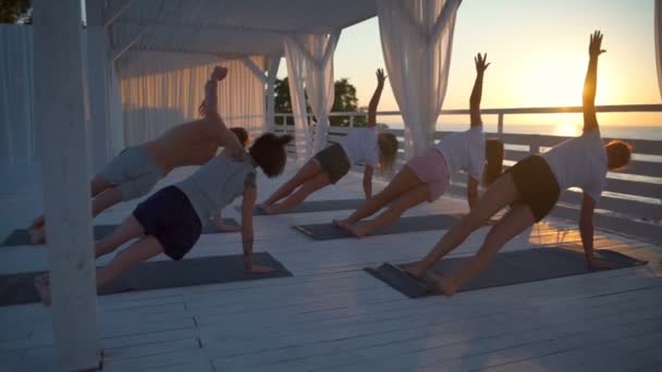 Young people practice yoga on terrace by the sea at dawn slow motion — Stock Video