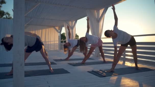 Groep jongeren doet yoga op terras in stralen van dawn slow motion — Stockvideo