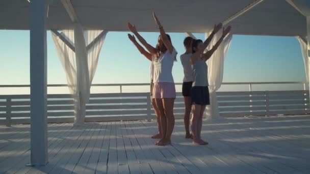 Vier Mädchen stehen im Kreis Rücken an Rücken und praktizieren Yoga im Morgengrauen in Zeitlupe — Stockvideo