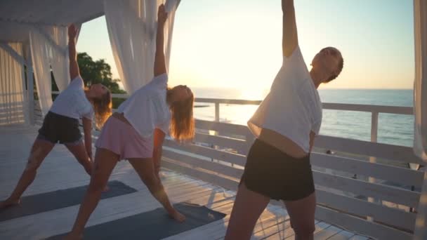 Three young female doing yoga on terrace by the sea at dawn slow motion — Stock Video