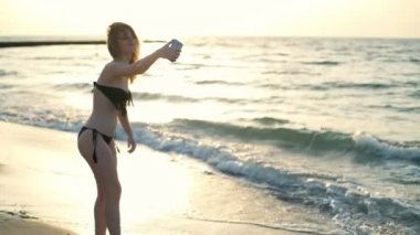 Genç güzel kız gülümseyerek, selfie Plajı'nda yapma Mayo içinde. Ağır çekim.