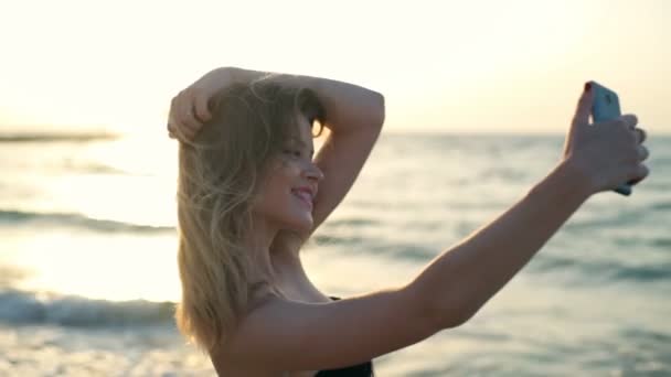 Mooi meisje met rode lippen in badmode lacht, selfie maken aan zee — Stockvideo