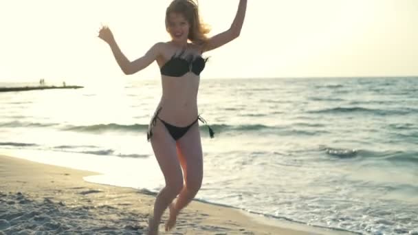 Joven chica hermosa en traje de baño sonriendo, saltando, caminando a la orilla del mar al amanecer — Vídeos de Stock