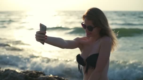 Junges schönes Mädchen in Badebekleidung und Sonnenbrille lächelt und macht Selfie — Stockvideo