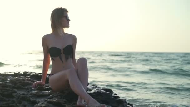Genç güzel kız gülümseyerek, sahil kayaya oturan mayo — Stok video