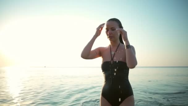 Young beautiful girl in swimwear smiling, going out of sea at sunrise — Stock Video