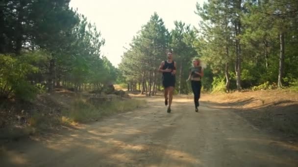 Couple sportif en vêtements de sport jogging souriant le long du chemin en forêt Mouvement lent — Video