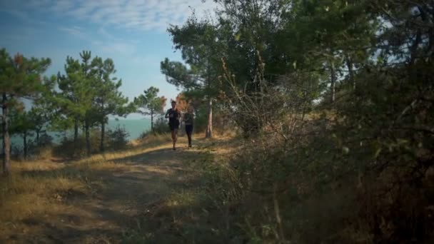 Casal esportivo correndo ao longo do caminho na floresta perto do mar Movimento lento — Vídeo de Stock