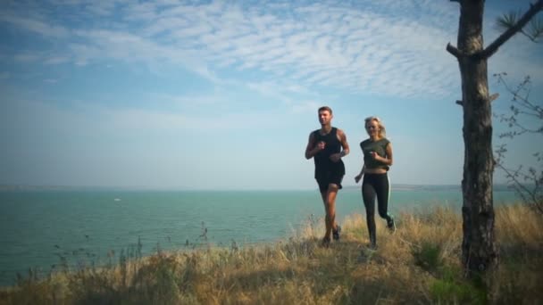 Sportovní dvojice s úsměvem, běhání na kopci nedaleko moře krajina Zpomalený pohyb — Stock video