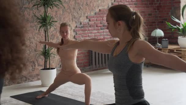 Jovem atraente fêmeas fazendo guerreiro postura no grande estúdio com instrutor — Vídeo de Stock