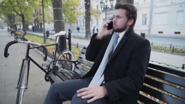 Hombre de negocios sentado en un banco hablando por teléfono — Vídeo de stock