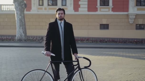 Bell'uomo d'affari in piedi su una piazza vicino alla bicicletta — Video Stock
