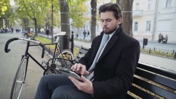 Бізнесмен використовує планшет, що сидить на лавці біля велосипеда — стокове відео