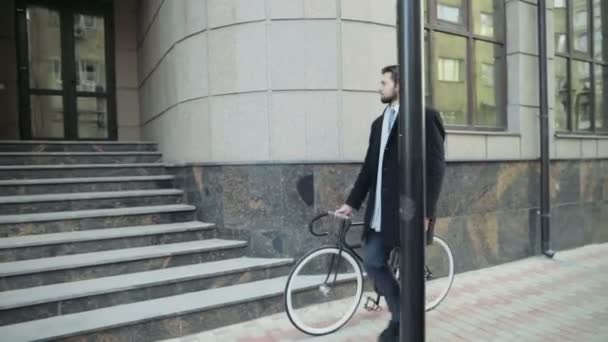 Homem de negócios bonito andando com sua bicicleta no centro da cidade — Vídeo de Stock