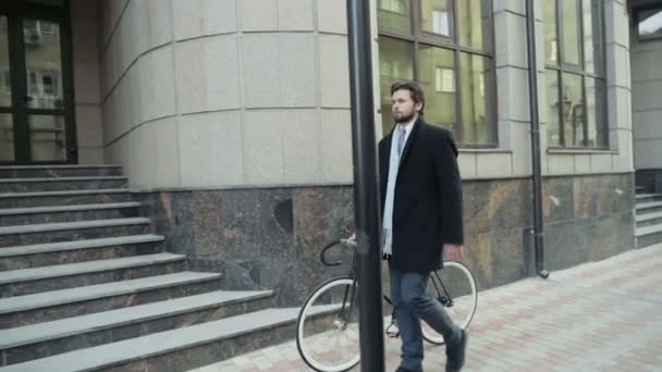 Hombre de negocios guapo caminando con su bicicleta en el centro de la ciudad — Vídeos de Stock