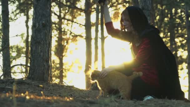 Κοκκινομάλλης μάγισσα χαϊδεύοντας μια γάτα τζίντζερ στο δάσος — Αρχείο Βίντεο