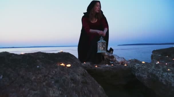 Jeune femme habillée comme une sorcière debout sur des rochers près du lac — Video