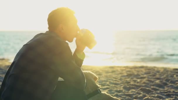 Молодий чоловік п'є з термоап на пляжі повільний рух — стокове відео