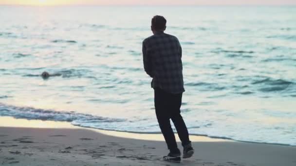 Молодой человек зовет свою собаку к берегу — стоковое видео