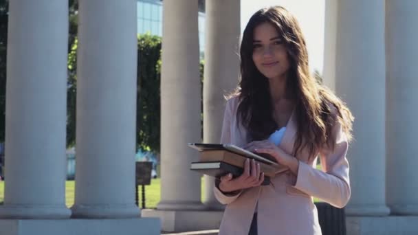 Smiling female student holding books and a tablet outdoors — Stock Video