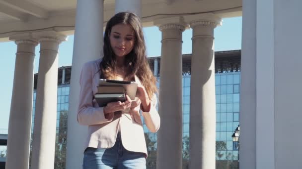 Estudiante mujer sosteniendo libros y usando una tableta al aire libre — Vídeos de Stock