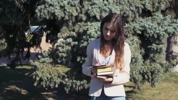 Estudiante femenina sosteniendo libros y usando una tableta en el parque — Vídeos de Stock