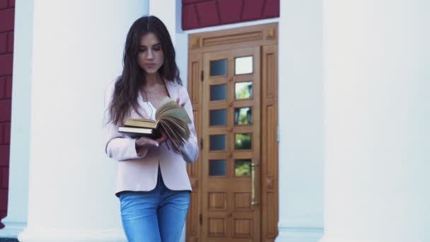 女子学生が大学のキャンパスの近くの本をめくって — ストック動画