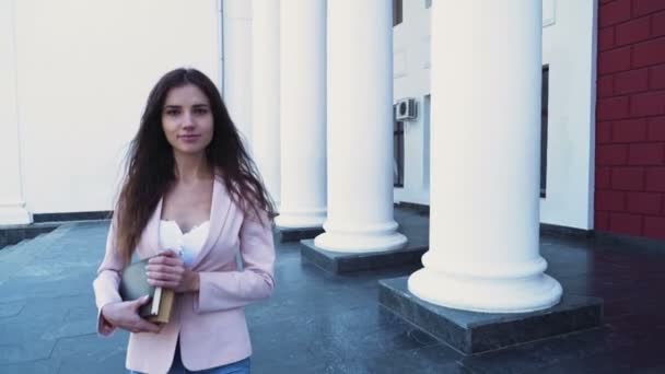 Vrouwelijke student houden boeken en lopen naar de camera op de campus — Stockvideo