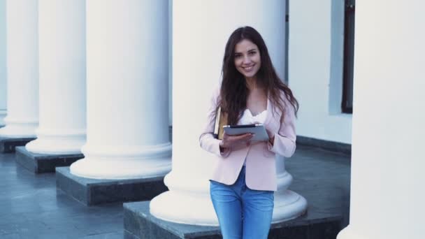 Smiling female student holding books and a tablet at the campus — Stock Video