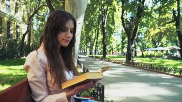 Estudante do sexo feminino lendo um livro em um banco no parque — Vídeo de Stock