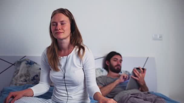 Écoute féminine de la musique dans les écouteurs et mâle à l'aide d'une tablette au lit — Video