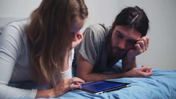 Homem e mulher usando um tablet enquanto deitado na cama — Vídeo de Stock