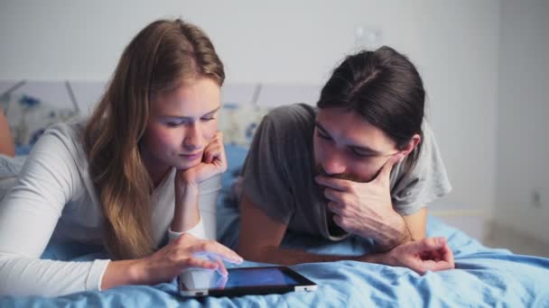 Homem e mulher usando um tablet enquanto deitado na cama — Vídeo de Stock