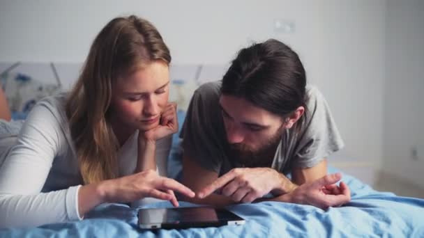 Hombre y mujer usando una tableta mientras están acostados en la cama — Vídeos de Stock