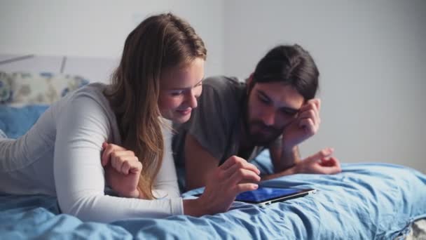 Hombre y mujer usando una tableta mientras están acostados en la cama — Vídeos de Stock