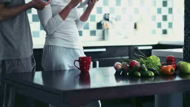 Mujer usando una tableta de pie en la cocina con el hombre sosteniendo una taza — Vídeo de stock