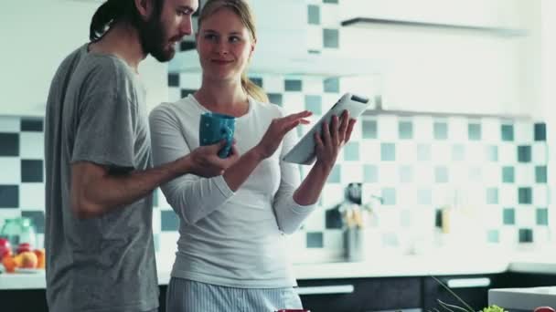 Vrouw met behulp van een Tablet PC-staande op de keuken met man met een kopje — Stockvideo