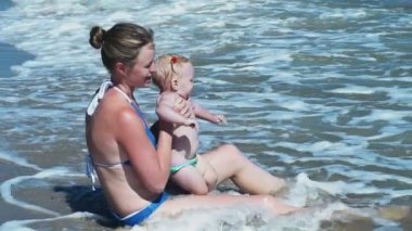Anne ve çocuğu su ağır çekimde sahilde oturmuş