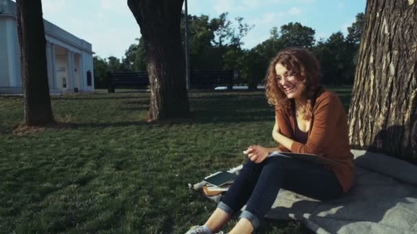 Πορτρέτο του ένα χαμογελαστό φοιτήτριας που κάθεται κάτω από το δέντρο στο πάρκο — Αρχείο Βίντεο