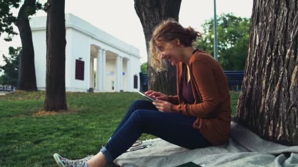 Vrouwelijke student zittend onder een boom in het park en het gebruik van Tablet PC — Stockvideo