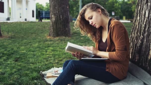 Estudante do sexo feminino lendo sob a árvore no parque câmera lenta — Vídeo de Stock