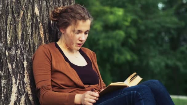 Female student reading under the tree in park slow motion — Stock Video