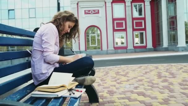 Estudante feminino sentado em um banco perto do edifício moderno câmera lenta — Vídeo de Stock