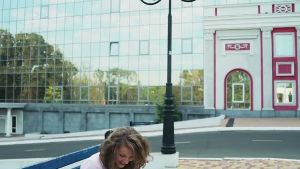 Estudante feminino sentado em um banco perto do edifício moderno câmera lenta — Vídeo de Stock