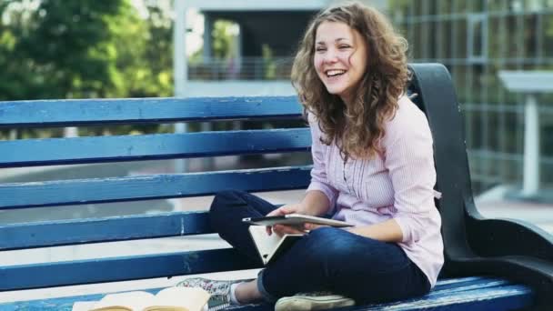 Feliz estudiante sentada en un banco y usando tableta cámara lenta — Vídeos de Stock