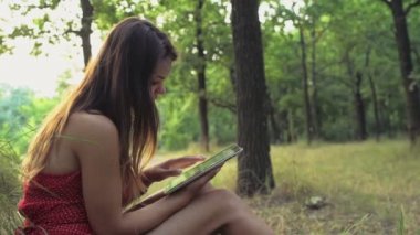 genç kadın bir ağacın oturur ve bir tablet bilgisayar yavaş kullanır
