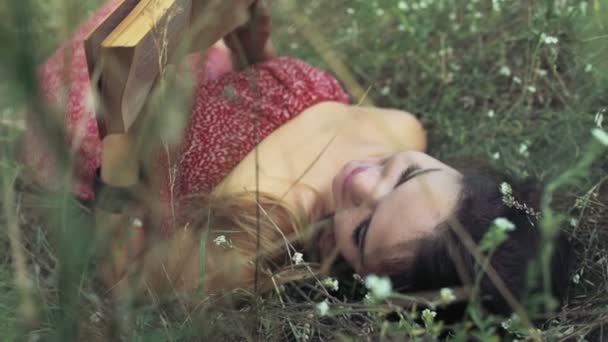 Молодая женщина лежит в полевых цветах и читает книгу замедленной съемки — стоковое видео