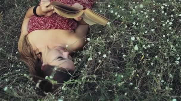 Jeune femme pose dans les fleurs des champs et lit un livre au ralenti — Video